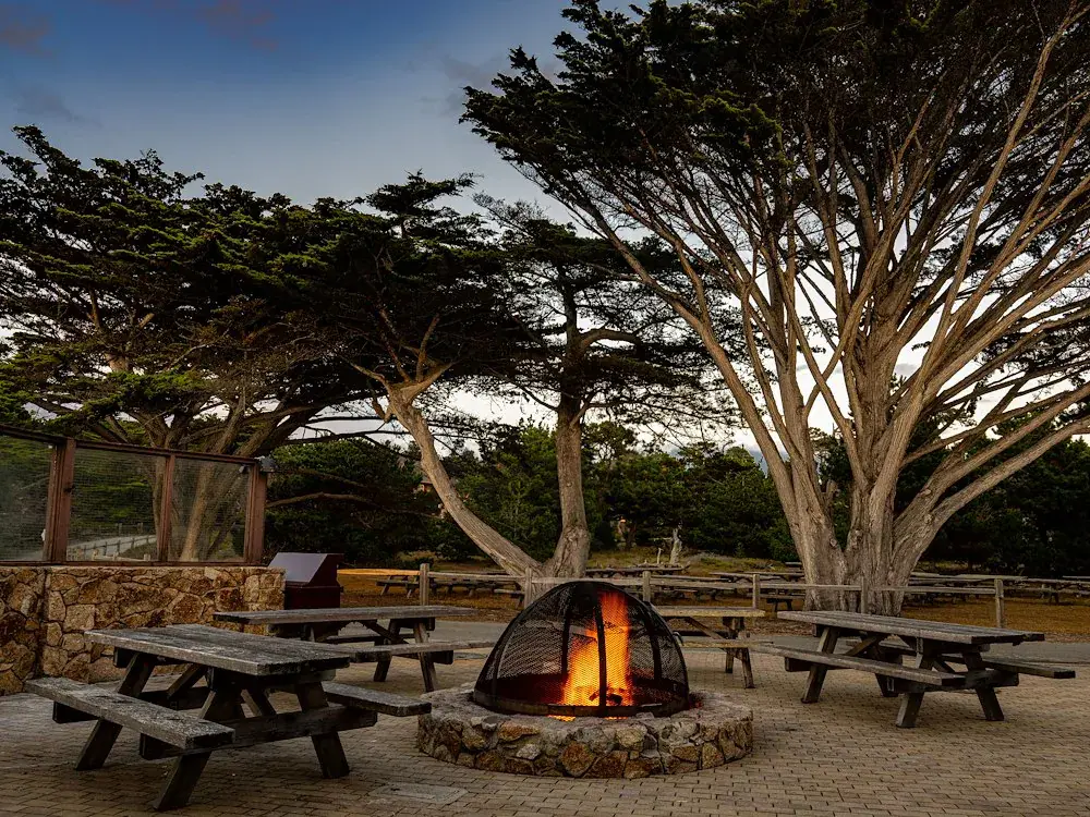 a-peaceful-outdoor-area-with-wooden-picnic-tables-surrounds-a-lit-fire-pit-asilomar-hotel-and-conference-grounds-pacific-grove-california